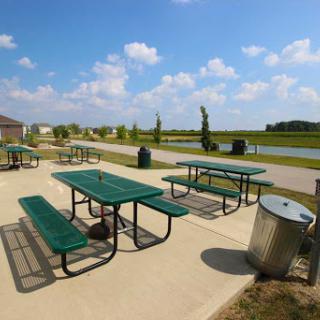 A serene park setting featuring green picnic tables under a bright blue sky.