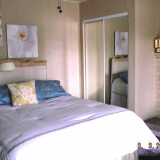 A cozy bedroom with a neatly made bed, decorative pillows, wall art, and a mirrored closet door.