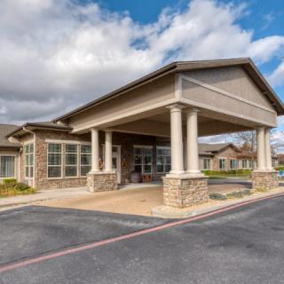A building with a covered entrance supported by columns and surrounded by a parking area.