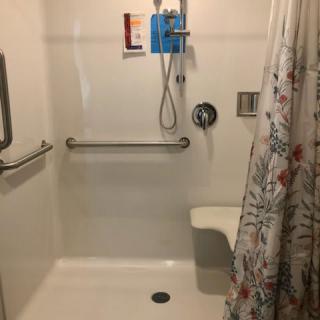 An accessible shower with handrails, a seat, and a floral curtain.