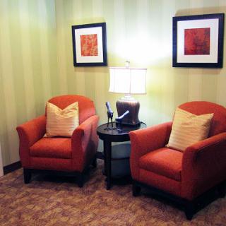 A cozy corner featuring two orange chairs, a side table, and wall art.