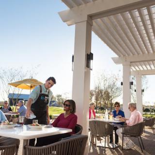 A waiter serves customers at an outdoor restaurant patio on a sunny day.