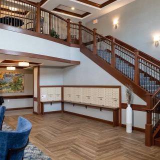 A stylish lobby interior featuring a modern staircase with wooden railings, mailboxes along the wall, and a comfortable seating area.