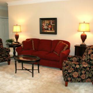 Elegant living room with a red sofa and floral armchairs, illuminated by matching lamps.