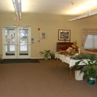 A welcoming lobby area featuring a table with floral arrangements, potted plants, and framed artwork near glass double doors.