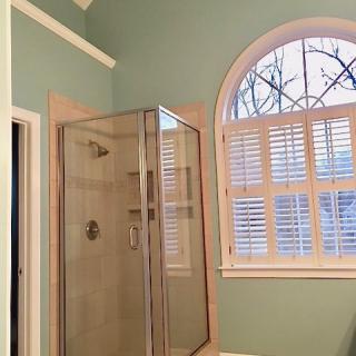 A bathroom with a glass shower and large arched window.
