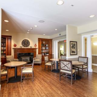 A cozy living area with tables, chairs, and a fireplace on wood flooring.