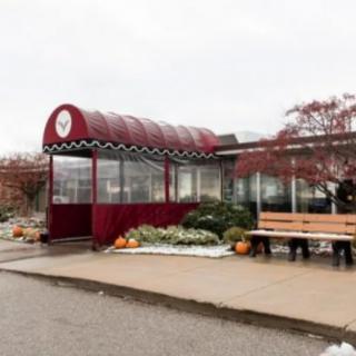 A cozy restaurant with a red awning and outdoor seating, adorned with autumn decorations including pumpkins.