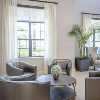 A modern living room with elegant armchairs, a round coffee table, large windows with curtains, and a potted plant.