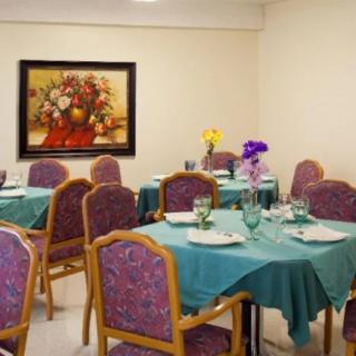 A cozy dining room with tables set for a meal, featuring teal tablecloths and floral decor.