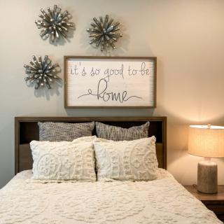A cozy bedroom setup with decorative pillows, wall art, and a bedside lamp.