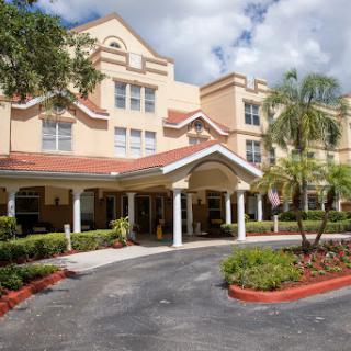 A welcoming entrance to a residential building surrounded by lush landscaping and palm trees.