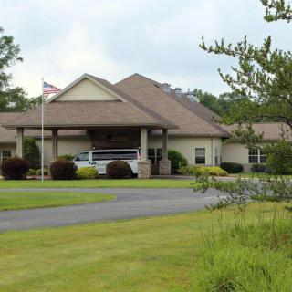 A single-story building with a driveway, surrounded by a well-maintained lawn and trees, featuring a flagpole at the front.