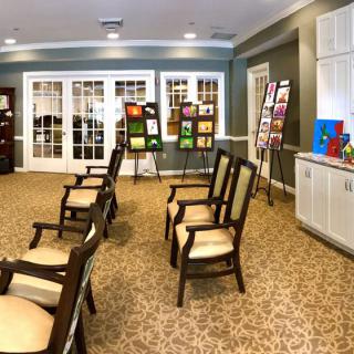An indoor art exhibition with paintings displayed on easels and chairs arranged for viewing.