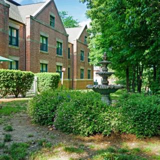 A brick building surrounded by lush greenery and a decorative fountain.