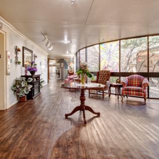 A well-decorated hallway with wooden flooring, featuring a table, chairs, artwork on the walls, and ample natural light.