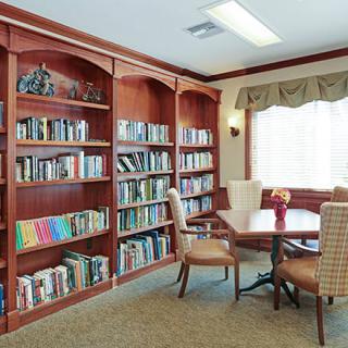 A cozy reading area with bookshelves and a table surrounded by chairs next to a window.
