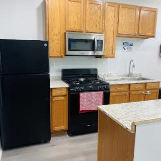 A modern kitchen featuring wooden cabinets, a black refrigerator, and stainless steel appliances.