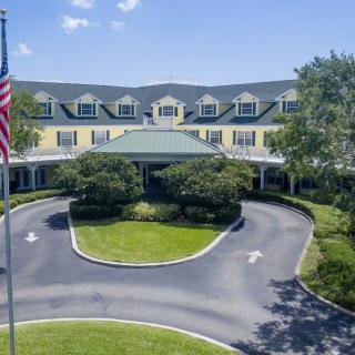 A large, elegant building with a circular driveway surrounded by trees and an American flag in the foreground.