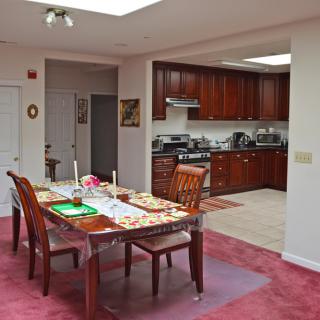 A view of a dining area with a table and chairs, adjacent to a kitchen with wooden cabinets and modern appliances.