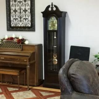 A cozy living room with a grandfather clock, piano, and comfortable couch.