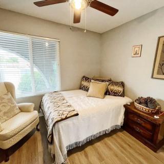 A cozy bedroom with a bed, armchair, and wooden nightstand under a ceiling fan.