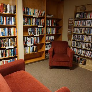 A cozy reading corner in a library, featuring shelves filled with books and a comfortable red chair.