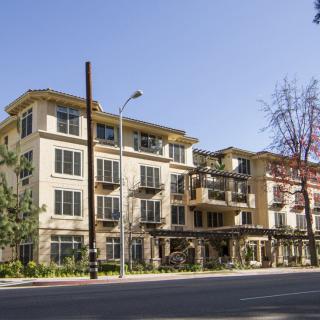 A modern apartment building with balconies viewed from across the street on a clear sunny day.