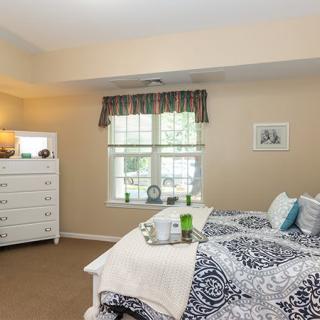 A cozy bedroom featuring a bed with patterned bedding, a white dresser, and a window with curtains.