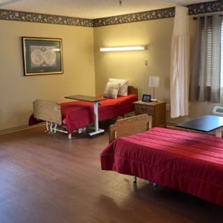 A well-organized bedroom with two beds, each covered with red bedspreads. The room features wooden flooring, curtains on the windows, and a decorative frame on the wall.