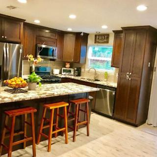 A modern kitchen with wooden cabinets and a granite countertop island, complete with bar stools and stainless steel appliances.