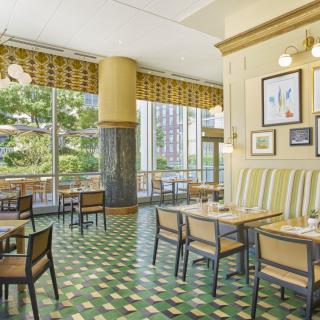 A bright and spacious restaurant interior with large windows, decorative artwork, and neatly arranged tables and chairs.