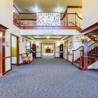 Spacious and welcoming lobby area with a central seating arrangement and carpeted flooring, featuring staircases on either side.