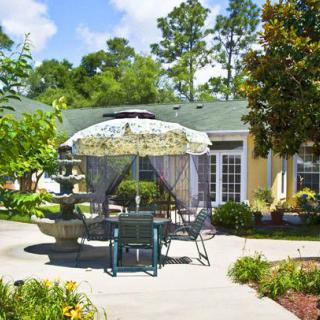 A serene garden patio with an umbrella, seating area, and fountain on a sunny day.