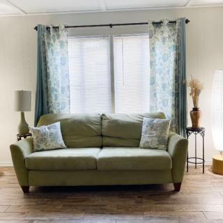 A cozy living room featuring a green sofa with patterned pillows, adorned by floral curtains and surrounded by stylish lamps.
