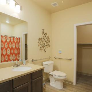 A well-lit bathroom featuring a sink, toilet, mirror, and a stylish orange shower curtain.