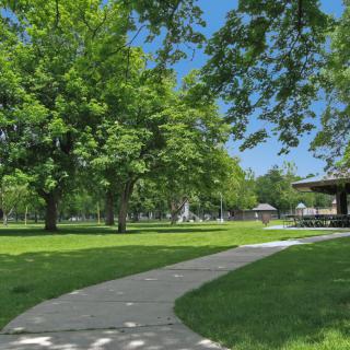 A sunny day in a park with lush green trees, a winding pathway, and a gazebo.