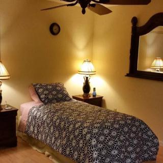 A cozy bedroom with a single bed, decorated with table lamps, a mirror, and a ceiling fan.