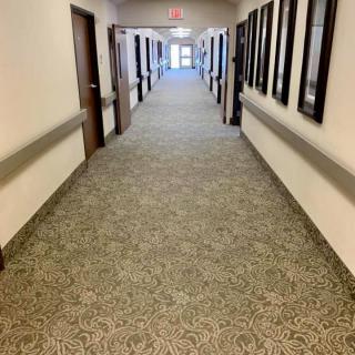 A long, carpeted hallway with multiple doors and ceiling lights.