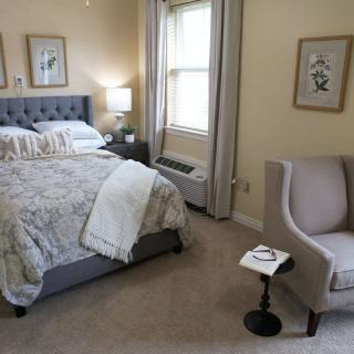 A cozy bedroom with a comfortable bed, stylish armchair, and warm lighting.