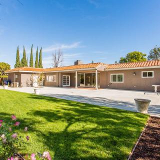 A beautiful backyard view of a single-story house with a well-maintained lawn and garden.