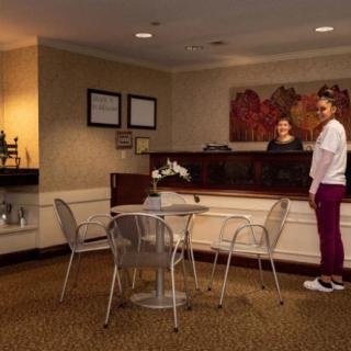 A receptionist assists a visitor in an office waiting area with modern decor and comfortable seating.