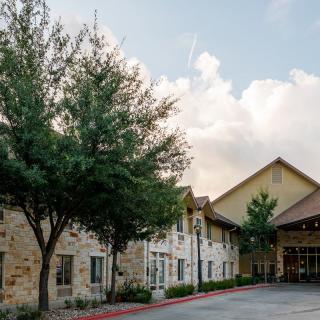 The exterior of a building with stone walls and trees lining the entrance under a cloudy sky.