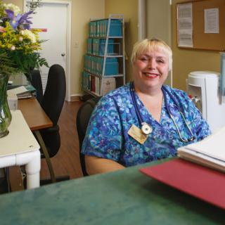 A friendly receptionist smiles at the camera in a welcoming office environment.