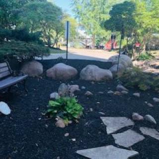 A serene garden landscape featuring a bench, pathway, and lush greenery.