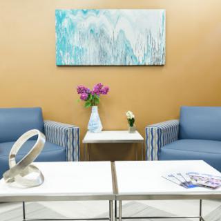 A cozy and modern waiting room featuring blue couches, floral decor, and contemporary artwork.