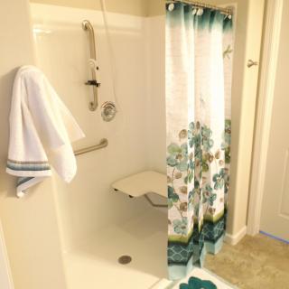A bathroom featuring a shower with a floral curtain, equipped with a grab bar and folding seat.