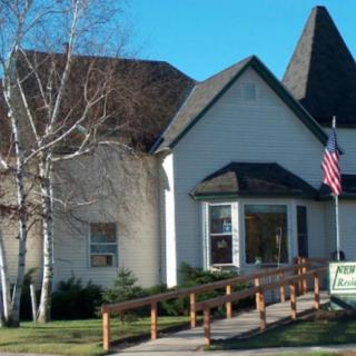A quaint white building with a pitched roof, housing a library, featuring an American flag and surrounded by trees.