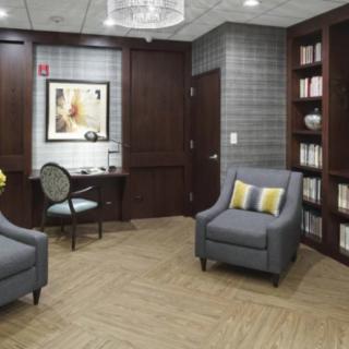 A cozy waiting room with comfortable chairs, a desk, and a bookshelf, complemented by artwork on the walls.