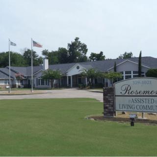 A view of an assisted living facility with a visible sign and surrounding greenery.